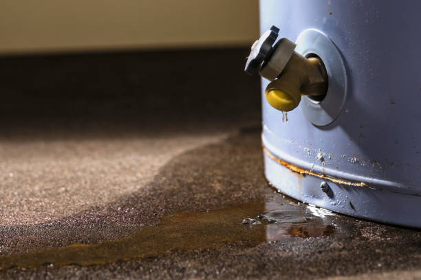Water leaking from the plastic faucet on a residential electric water heater sitting on a concrete floor.